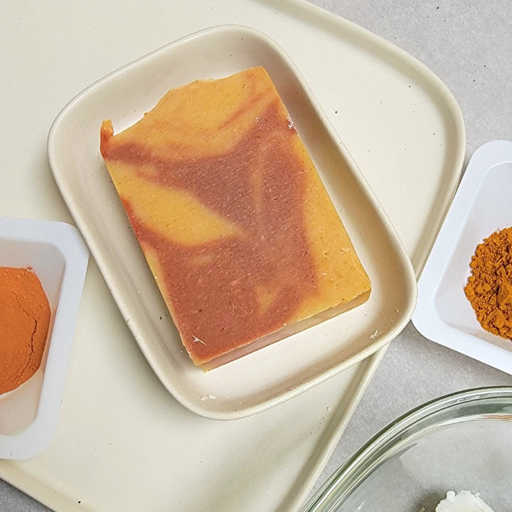 Handmade Turmeric & Lemongrass Soap – Radiance & Skin Renewal
Packed with turmeric’s skin-brightening benefits, this small-batch, handcrafted soap gently purifies and nourishes the skin. Himalayan rhubarb root and Brazilian red clay help to even out skin tone, while kaolin clay detoxifies without drying. Scented with an uplifting blend of lemongrass, ylang ylang, ho wood, and turmeric essential oils, this luxurious soap offers an energizing yet soothing cleanse.